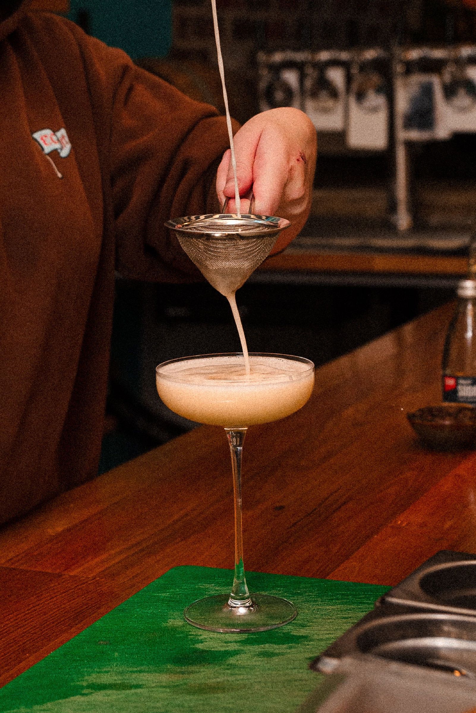 A cocktail being strained into a coupe on the bar